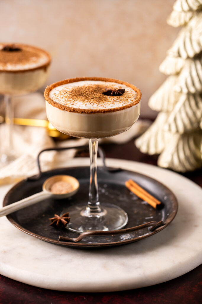 A full view of a glass of Eggnog with star of anise in the center sprinkled with cinnamon.