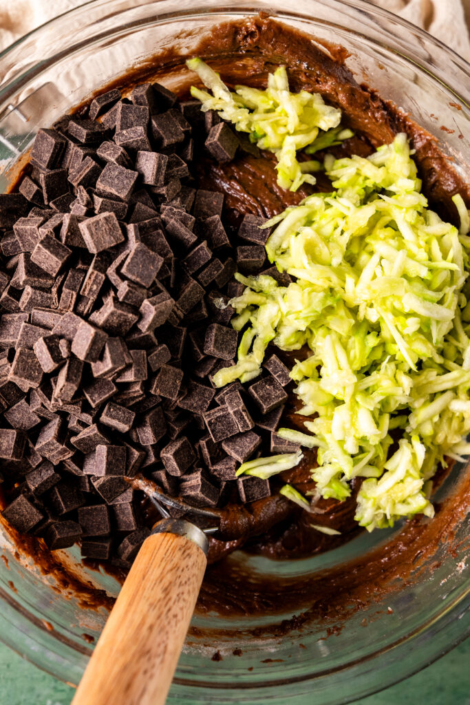 zucchini chocolate muffin batter in a bowl with chocolate chips and shredded zucchini added