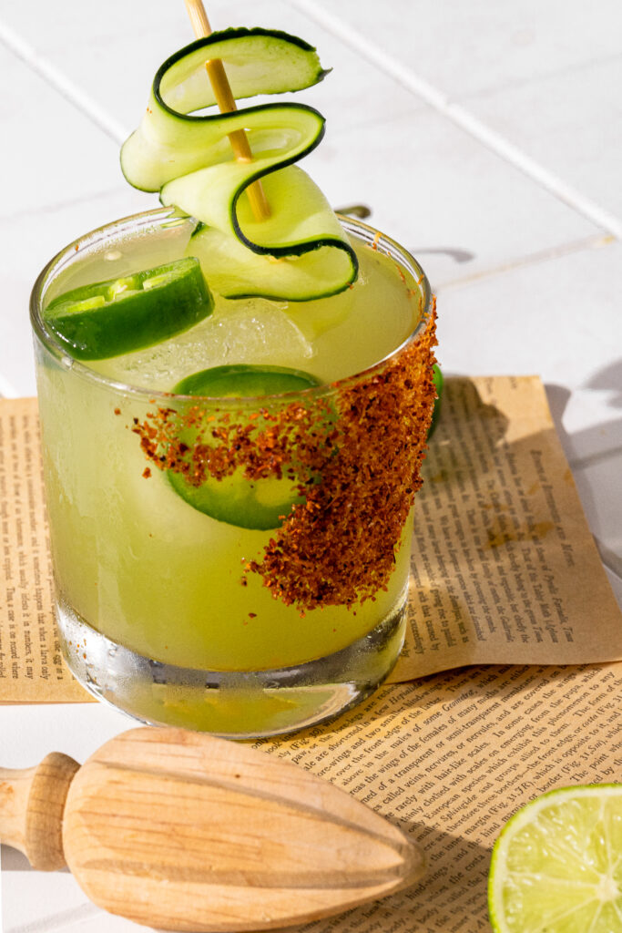 A close up detailed photo of the cucumber jalapeno margarita where you can easily see the fresh jalapeños and cucumbers along with tajin. 