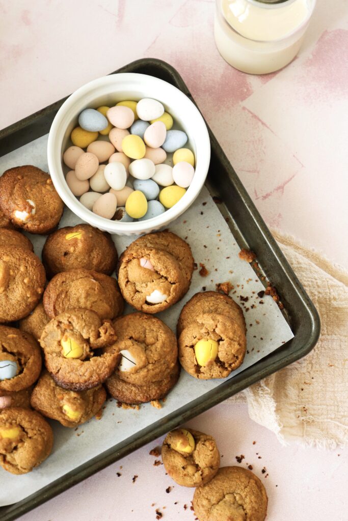 A side shot of the baking sheet filled with the cookies and a small bowl filled with the gluten-free mini chocolate eggs.