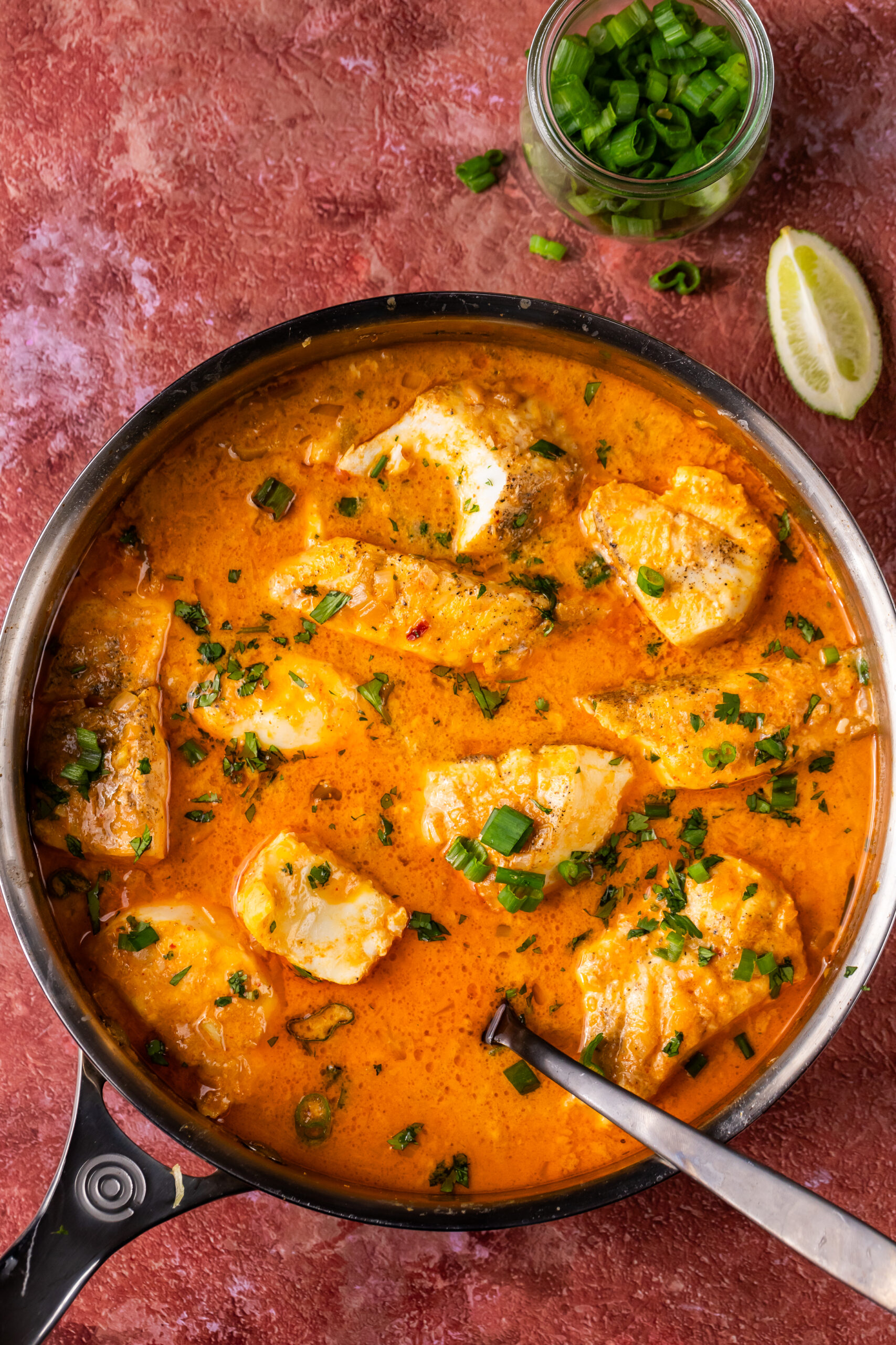 A full bowl filled with the Thai-Style Halibut in coconut curry broth accompanied by a lemon wedge and chives for garnish.